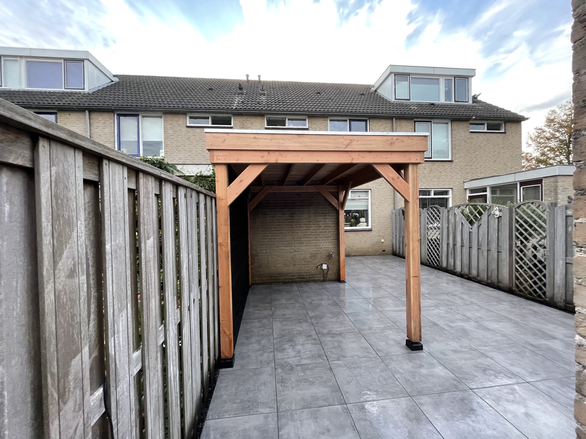 Houten overkapping op een betegeld terras achter een rijtjeshuis, met houten schutting